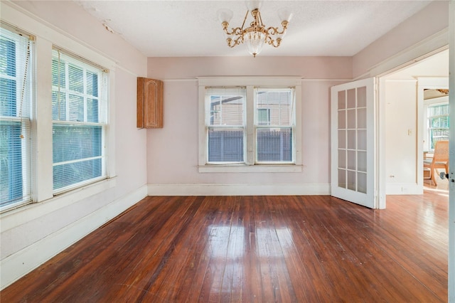 spare room with plenty of natural light, a chandelier, and dark hardwood / wood-style flooring