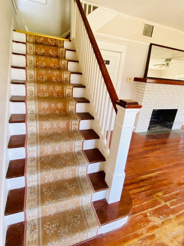 stairs featuring hardwood / wood-style floors, ceiling fan, and a fireplace