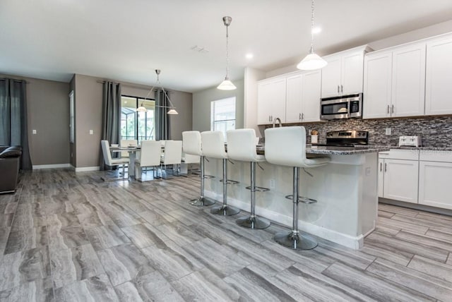 kitchen featuring a kitchen bar, appliances with stainless steel finishes, white cabinets, hanging light fixtures, and a kitchen island with sink