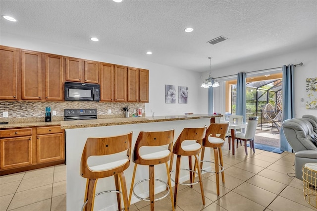 kitchen featuring a notable chandelier, a kitchen island, pendant lighting, a breakfast bar, and black appliances