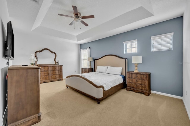 bedroom featuring ceiling fan, light carpet, a tray ceiling, and a textured ceiling