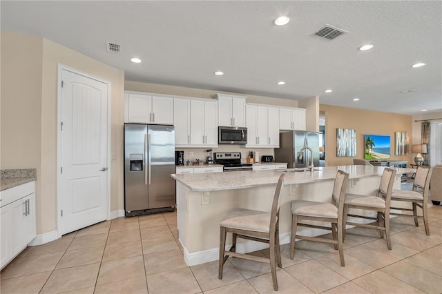 kitchen featuring appliances with stainless steel finishes, white cabinetry, light stone counters, and a center island with sink