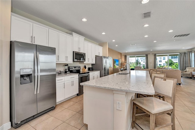 kitchen with an island with sink, sink, white cabinets, appliances with stainless steel finishes, and a breakfast bar