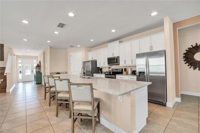 kitchen featuring an island with sink, stainless steel appliances, a kitchen breakfast bar, white cabinetry, and light stone counters