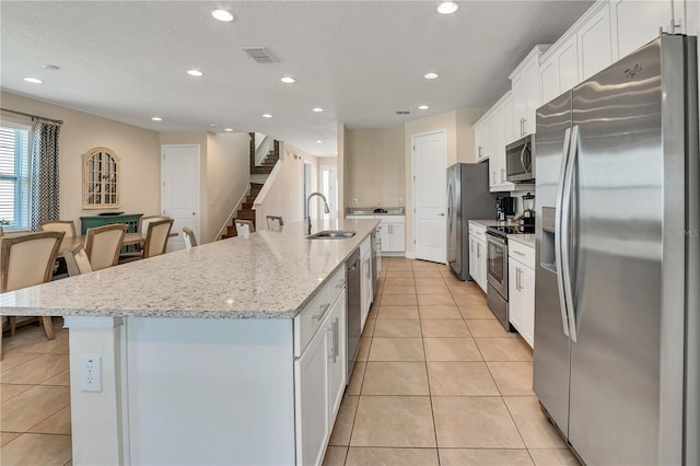 kitchen with an island with sink, light stone countertops, appliances with stainless steel finishes, white cabinetry, and sink