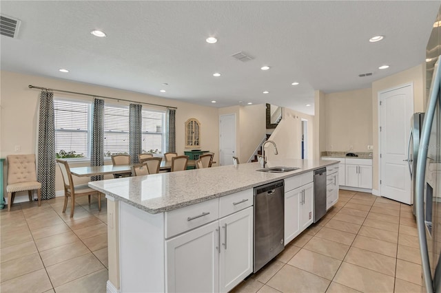 kitchen with light stone countertops, sink, stainless steel appliances, an island with sink, and white cabinets