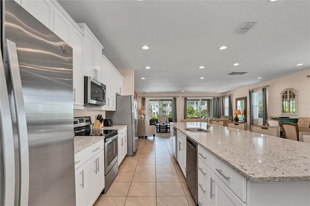 kitchen with an island with sink, stainless steel appliances, light tile floors, sink, and white cabinets