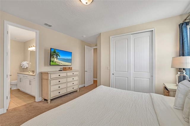 carpeted bedroom with a textured ceiling, ensuite bathroom, and a closet