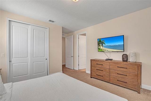 bedroom with a textured ceiling, a closet, and light colored carpet