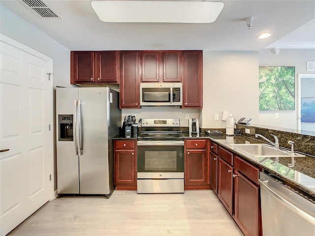 kitchen featuring light hardwood / wood-style floors, ornamental molding, dark stone countertops, appliances with stainless steel finishes, and sink