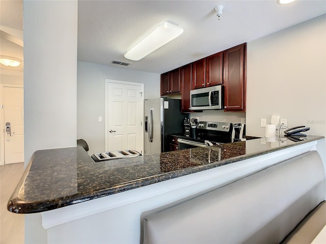 kitchen featuring appliances with stainless steel finishes, dark stone counters, kitchen peninsula, hardwood / wood-style floors, and a kitchen bar