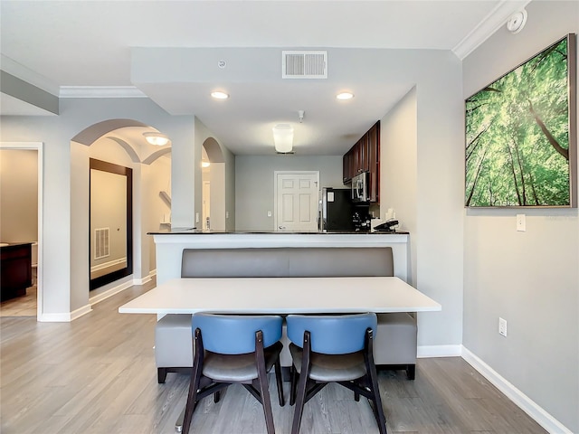 kitchen featuring light hardwood / wood-style floors, kitchen peninsula, fridge, dark brown cabinetry, and a breakfast bar area