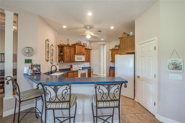 kitchen with white appliances, a kitchen bar, ceiling fan, and kitchen peninsula