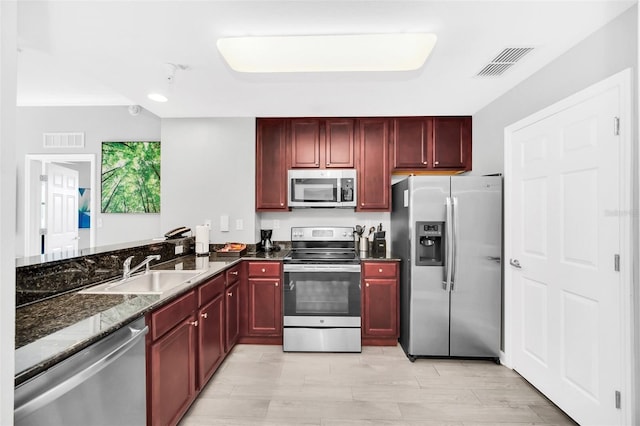 kitchen with kitchen peninsula, dark stone countertops, sink, and appliances with stainless steel finishes