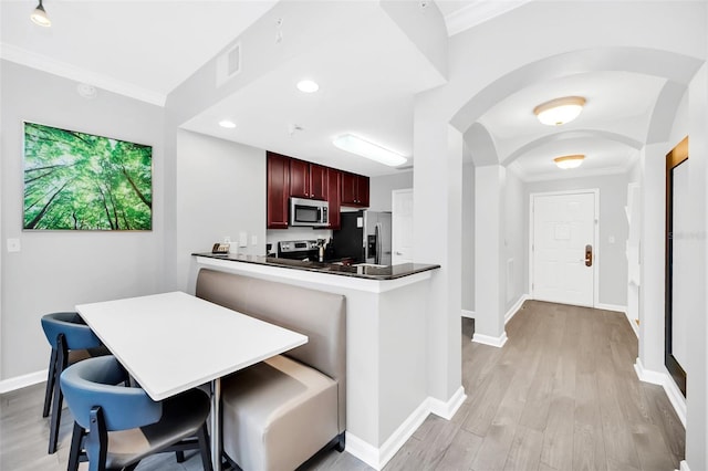 kitchen with kitchen peninsula, light wood-type flooring, a breakfast bar, stainless steel appliances, and crown molding