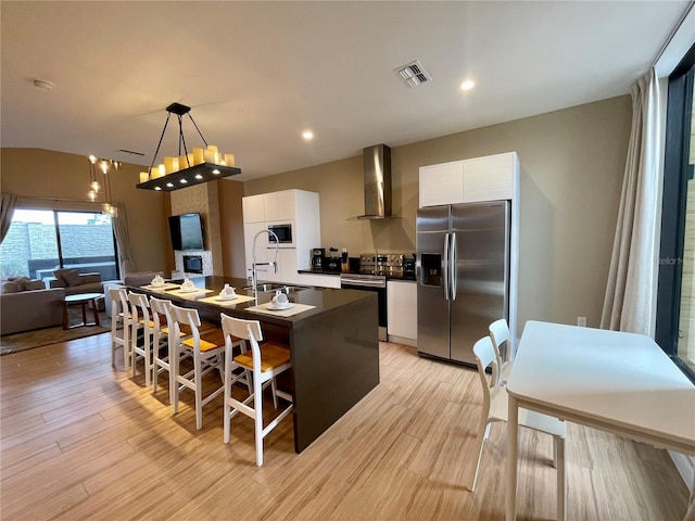 kitchen featuring visible vents, a sink, stainless steel appliances, white cabinets, and wall chimney range hood