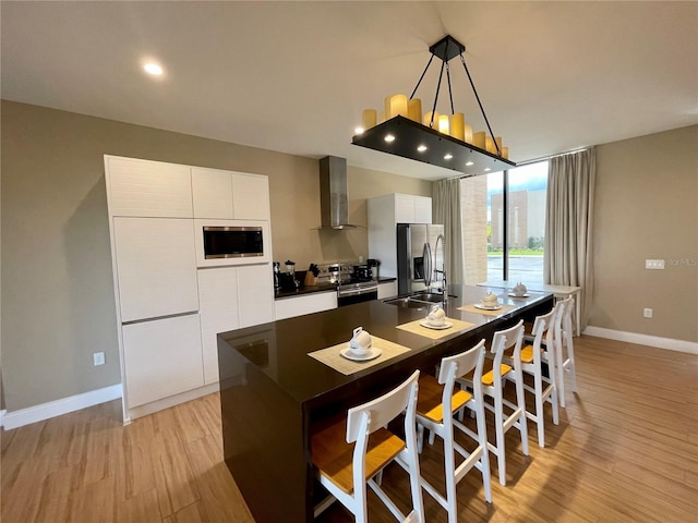 kitchen with appliances with stainless steel finishes, light hardwood / wood-style flooring, a kitchen island, white cabinetry, and wall chimney exhaust hood