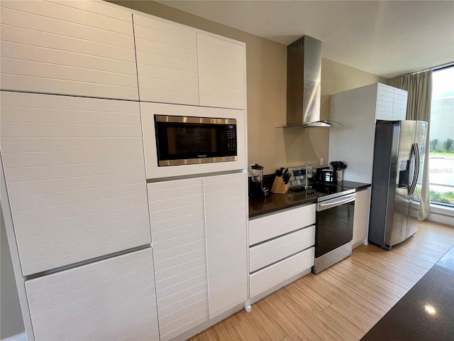 kitchen featuring appliances with stainless steel finishes, dark countertops, exhaust hood, modern cabinets, and light wood-type flooring