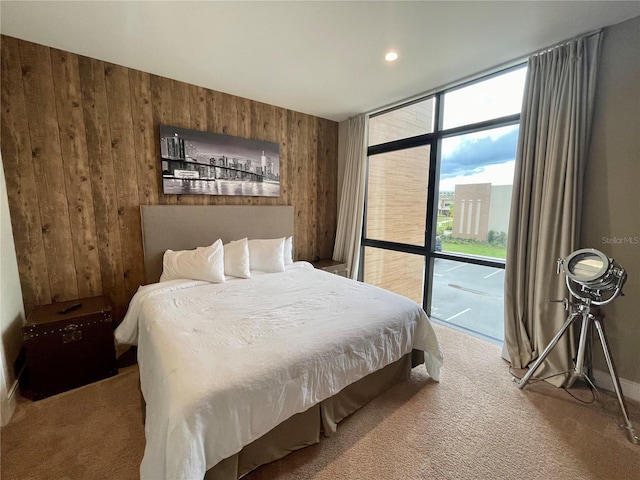 bedroom featuring a wall of windows, access to outside, wood walls, and light carpet