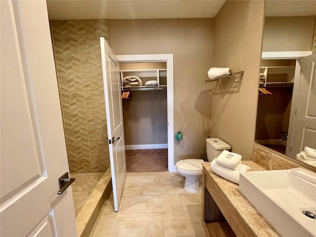 bathroom featuring tile patterned flooring, a walk in closet, toilet, tiled shower, and vanity