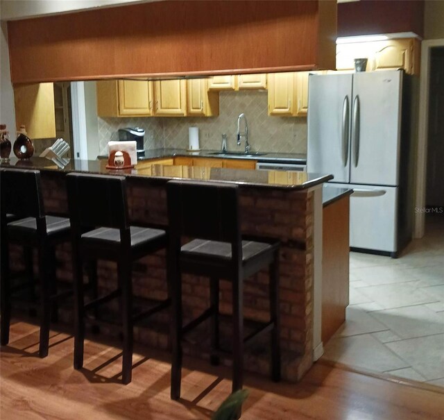 kitchen featuring sink, a kitchen bar, stainless steel refrigerator, and light wood-type flooring