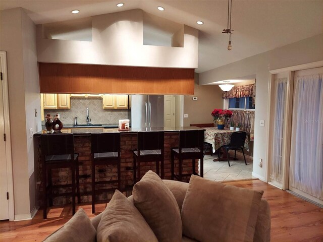 interior space featuring sink, a kitchen breakfast bar, light hardwood / wood-style flooring, stainless steel refrigerator, and tasteful backsplash