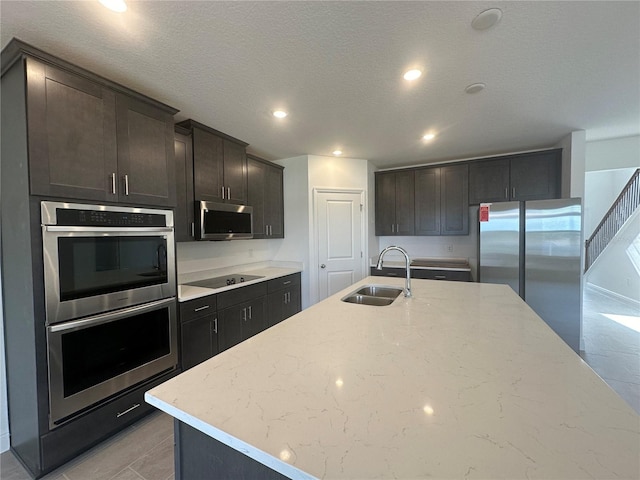 kitchen featuring light stone counters, a kitchen island with sink, stainless steel appliances, sink, and a textured ceiling