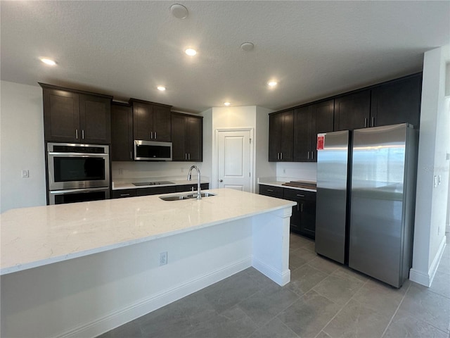 kitchen with light stone countertops, a kitchen island with sink, stainless steel appliances, and sink