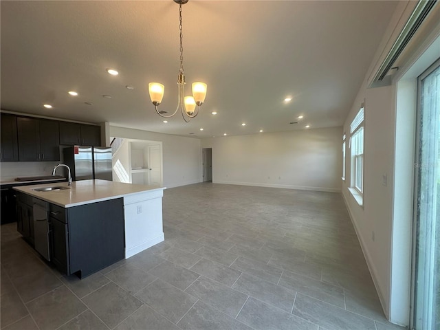 kitchen with stainless steel refrigerator, a kitchen island with sink, a chandelier, pendant lighting, and sink