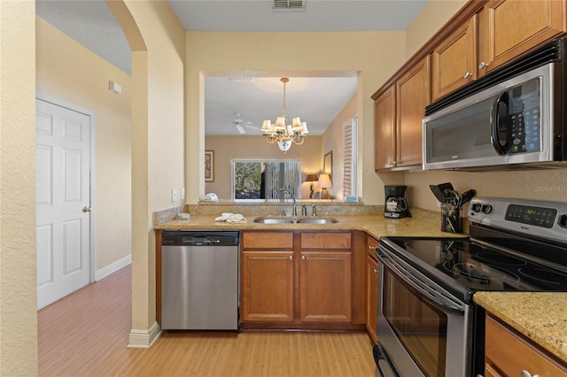 kitchen featuring sink, an inviting chandelier, stainless steel appliances, light stone countertops, and light wood-type flooring