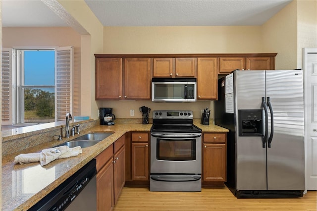 kitchen with stainless steel appliances, light stone countertops, sink, and light hardwood / wood-style floors