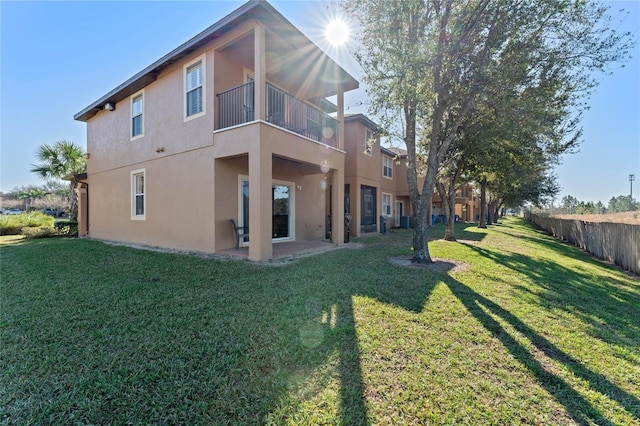 back of house with a balcony, a patio area, and a lawn