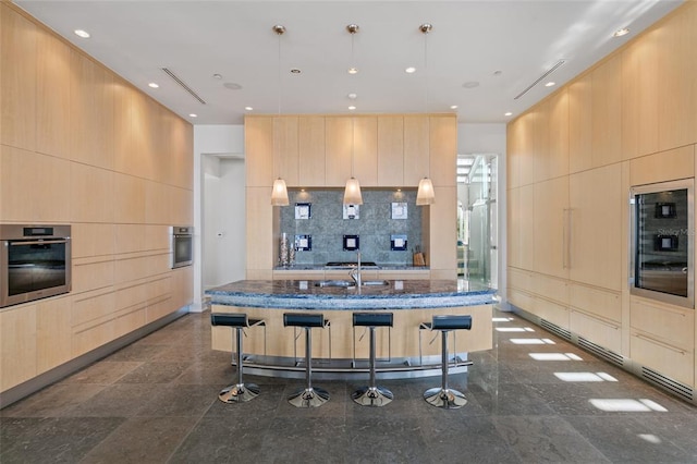 kitchen with pendant lighting, a kitchen breakfast bar, oven, a kitchen island with sink, and dark stone countertops