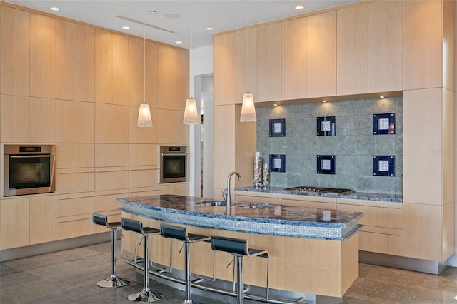 kitchen with dark stone countertops, a center island with sink, decorative light fixtures, and appliances with stainless steel finishes