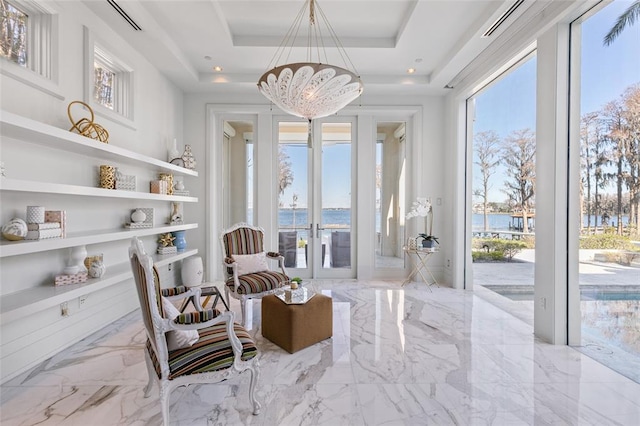 living area with light tile floors, french doors, a water view, a raised ceiling, and an inviting chandelier