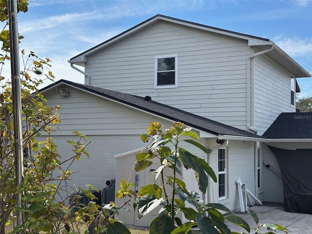 view of property exterior with roof with shingles and a patio