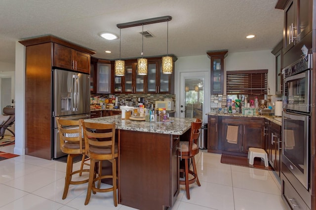 kitchen with light tile patterned floors, stainless steel appliances, visible vents, backsplash, and a center island