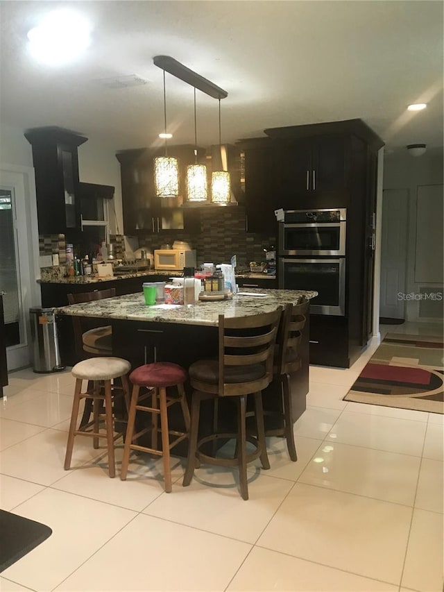 bar with decorative backsplash, white microwave, stainless steel double oven, pendant lighting, and light tile patterned flooring