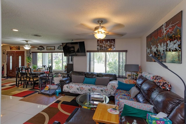 living room featuring light tile patterned floors, ceiling fan, visible vents, and a textured ceiling