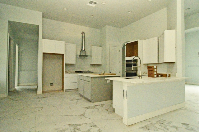 kitchen with sink, a kitchen island with sink, white cabinetry, ventilation hood, and stainless steel oven