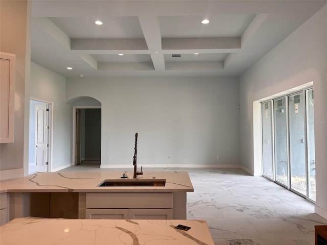 kitchen with sink, a towering ceiling, coffered ceiling, light stone counters, and beamed ceiling