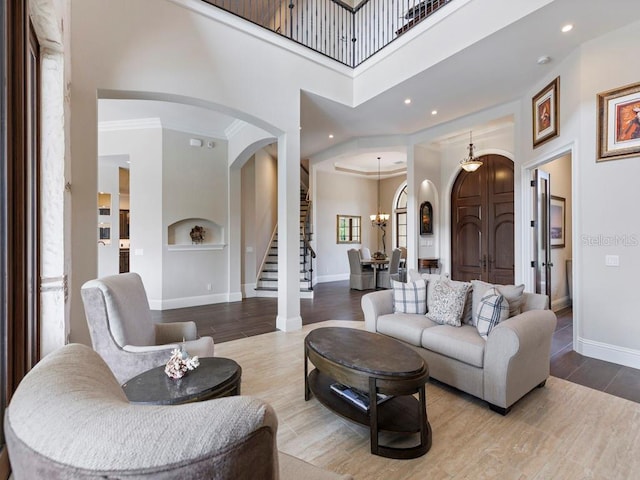 living room featuring a high ceiling, a notable chandelier, light hardwood / wood-style floors, built in shelves, and crown molding