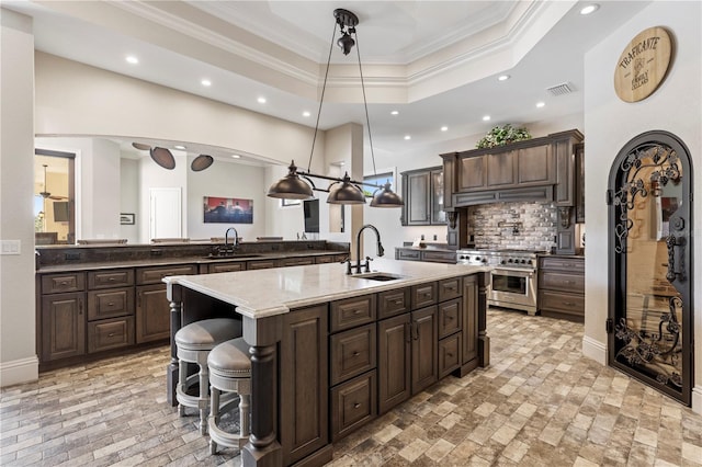 kitchen featuring a kitchen bar, a center island with sink, range with two ovens, hanging light fixtures, and sink