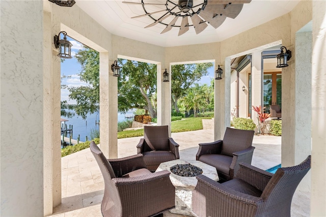 view of patio with a water view, ceiling fan, and an outdoor living space with a fire pit