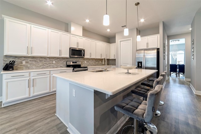 kitchen featuring an island with sink, pendant lighting, sink, appliances with stainless steel finishes, and white cabinetry