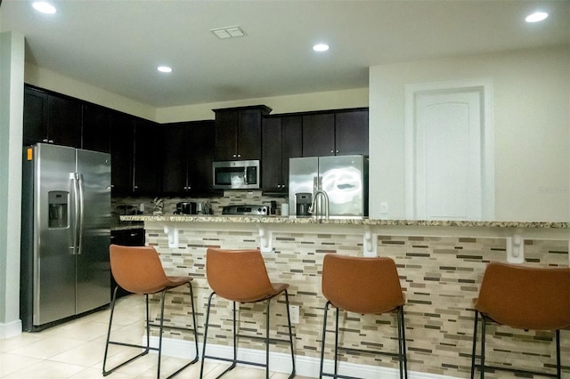 kitchen with light stone countertops, sink, stainless steel appliances, light tile floors, and tasteful backsplash