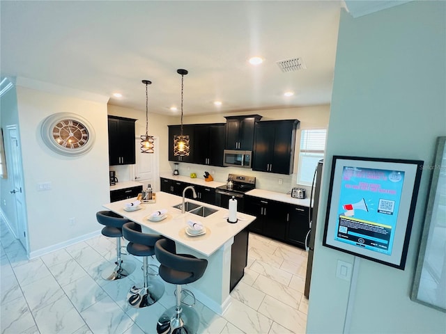 kitchen with an island with sink, a breakfast bar, appliances with stainless steel finishes, hanging light fixtures, and sink