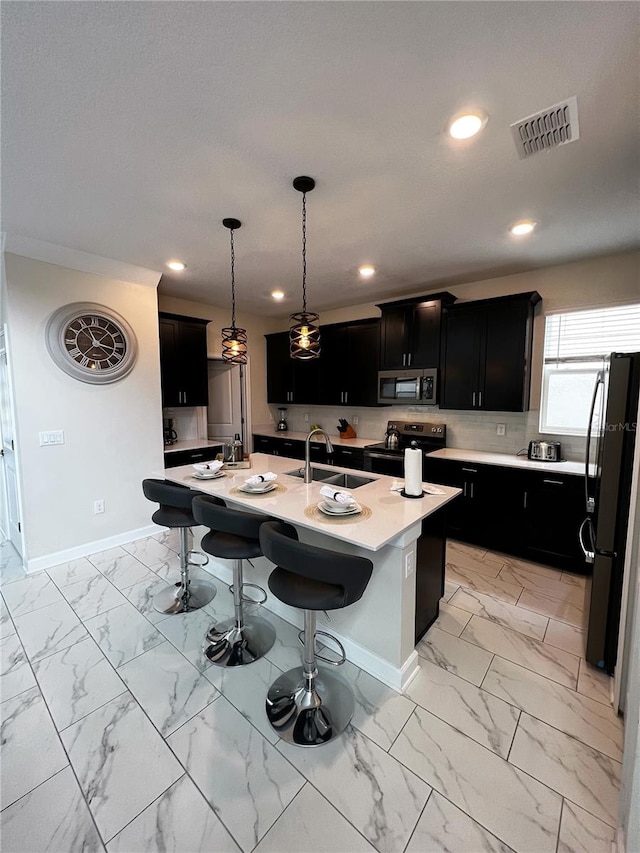 kitchen featuring sink, hanging light fixtures, a breakfast bar area, a center island with sink, and stainless steel appliances