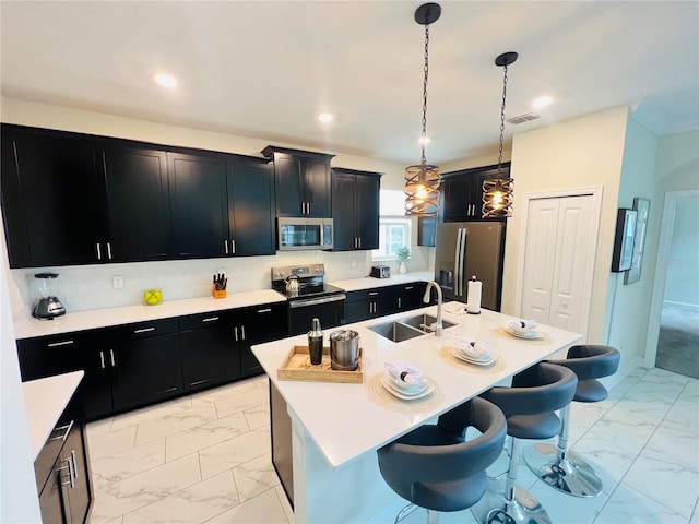 kitchen with stainless steel appliances, decorative light fixtures, a center island with sink, a breakfast bar area, and sink