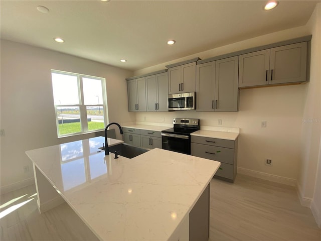 kitchen with light stone counters, sink, a center island with sink, and appliances with stainless steel finishes